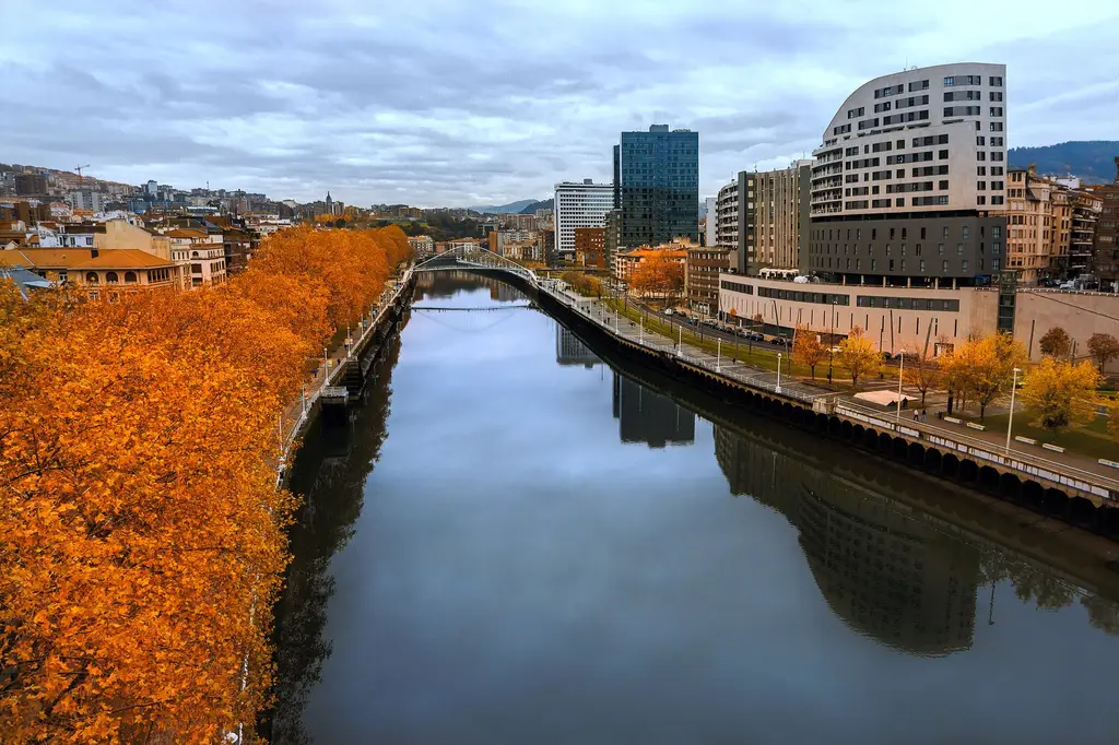Bilbao: Autumn view of a river in Bilbao, Spain with orange foliage and modern skyline.