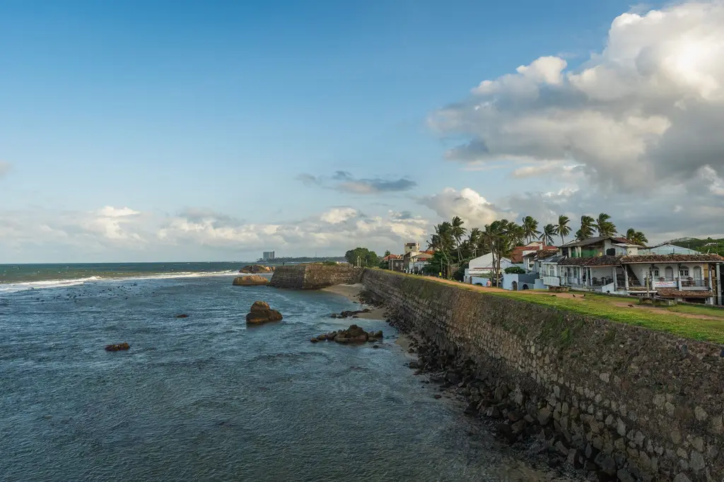 Sri Lanka: Picturesque seaside view of the historic Galle Fort in Sri Lanka, featuring the coastal wall and ocean under a cloudy sky.
