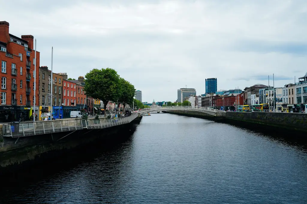 Dublin: Scenic view of Dublin's Ha'penny Bridge over the River Liffey amidst urban architecture and vibrant city life.