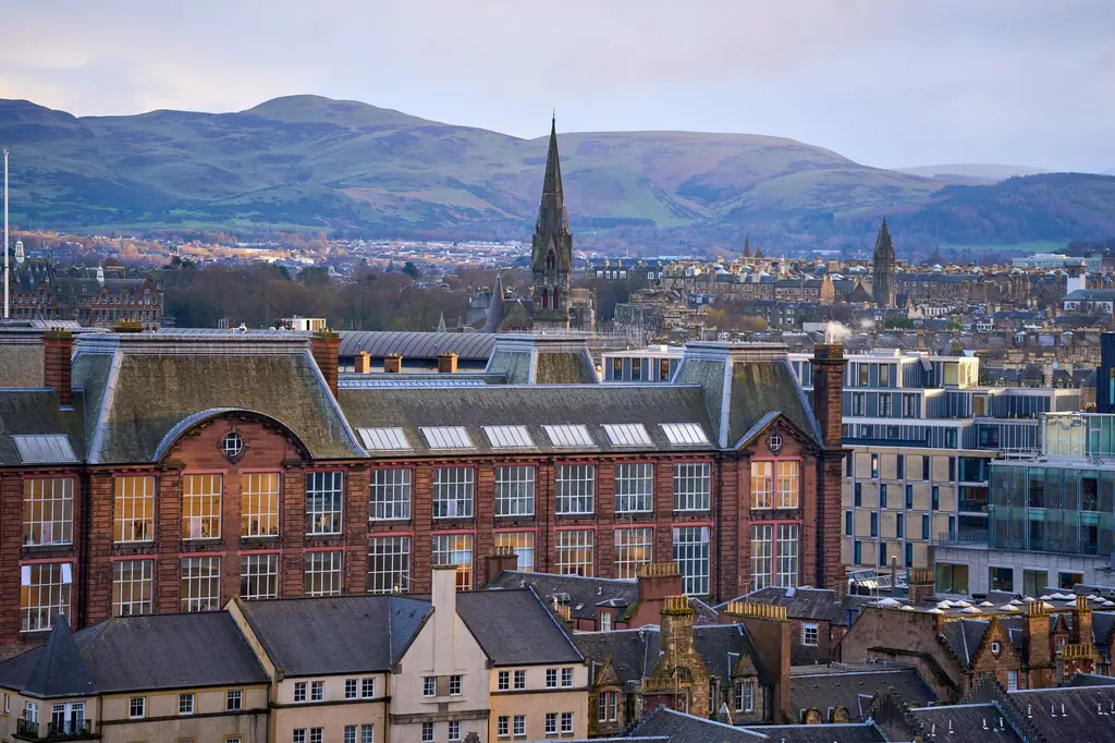 Edinburgh: Edinburgh cityscape featuring historic architecture and surrounding hills at sunset.