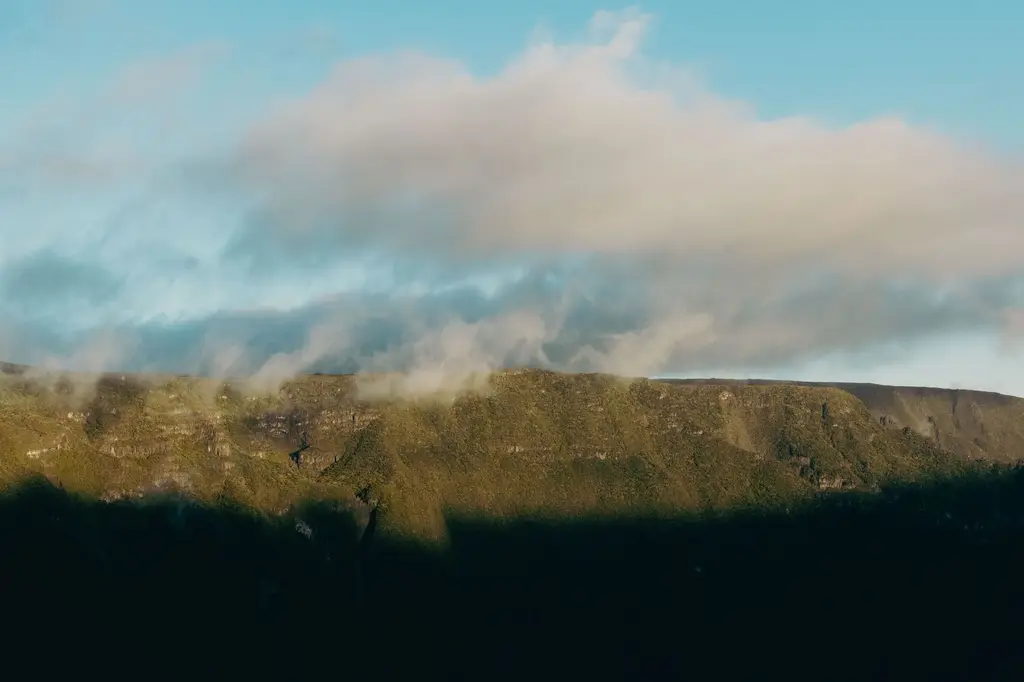 La Réunion: A stunning view of lush green mountains with clouds at sunrise in La Réunion, France.