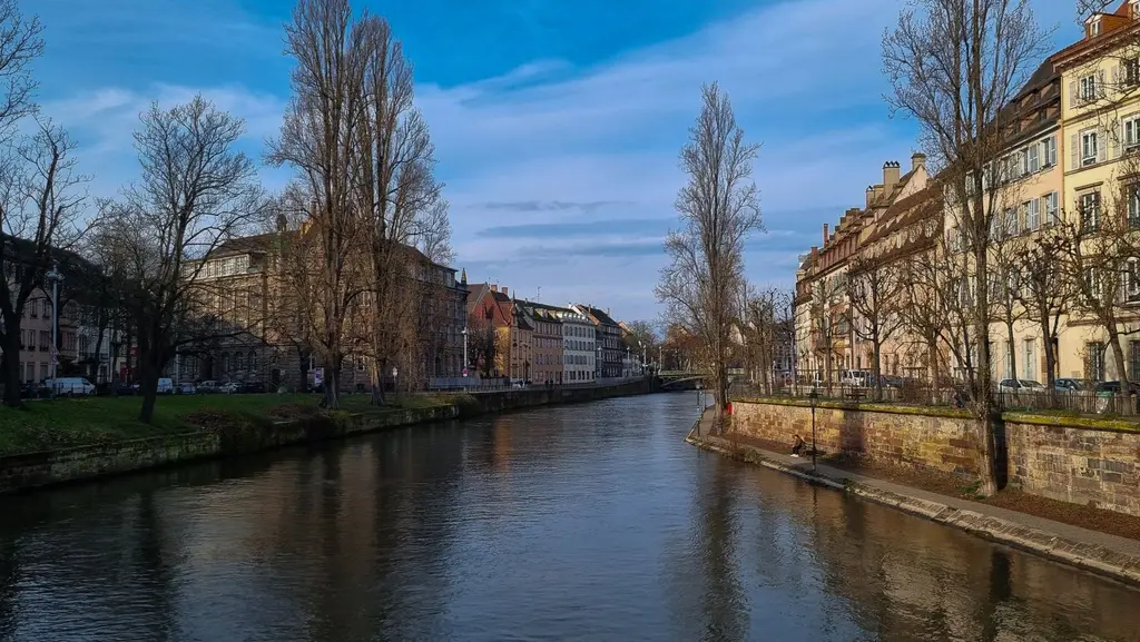 Strasbourg: Serene view of Strasbourg canal flanked by historic buildings and bare trees under a bright winter sky.